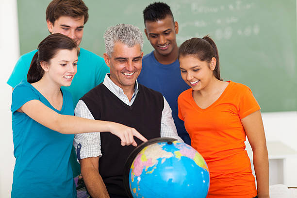 A teacher and four students stand around a globe in a classroom, with one student pointing at a location, highlighting the Top 7 Skills Students Gain from the IGCSE Curriculum through interactive learning.