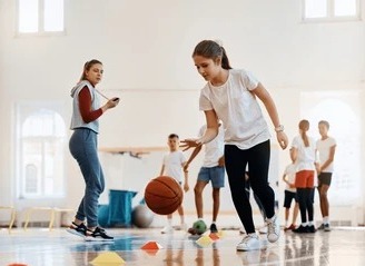 Young individuals playing basketball in an indoor gym, highlighting an active physical education environment.
